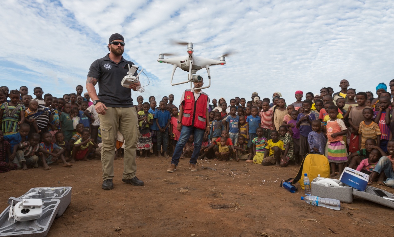 A man flies a drone in front of a group of children